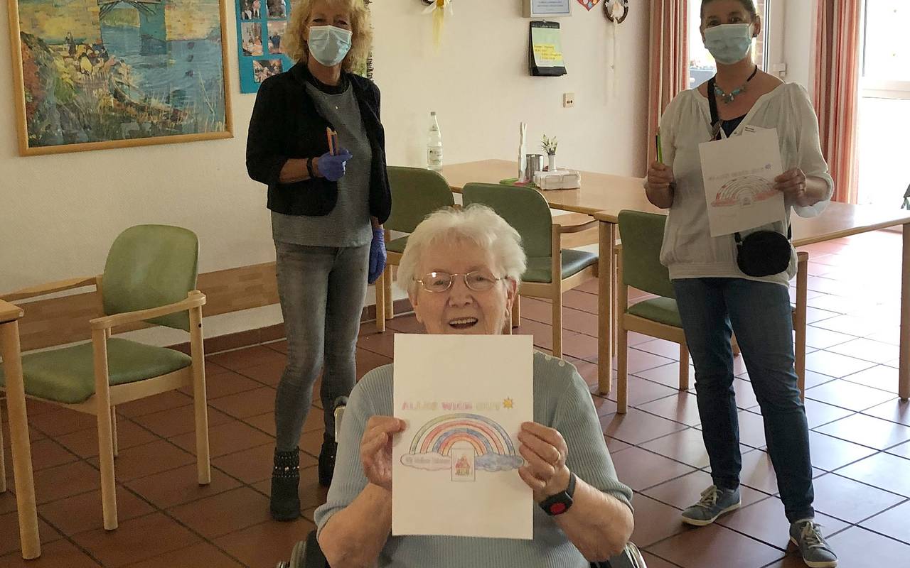Senioren hält einen Zettel in die Kamera, da ist ein Regenbogen drauf