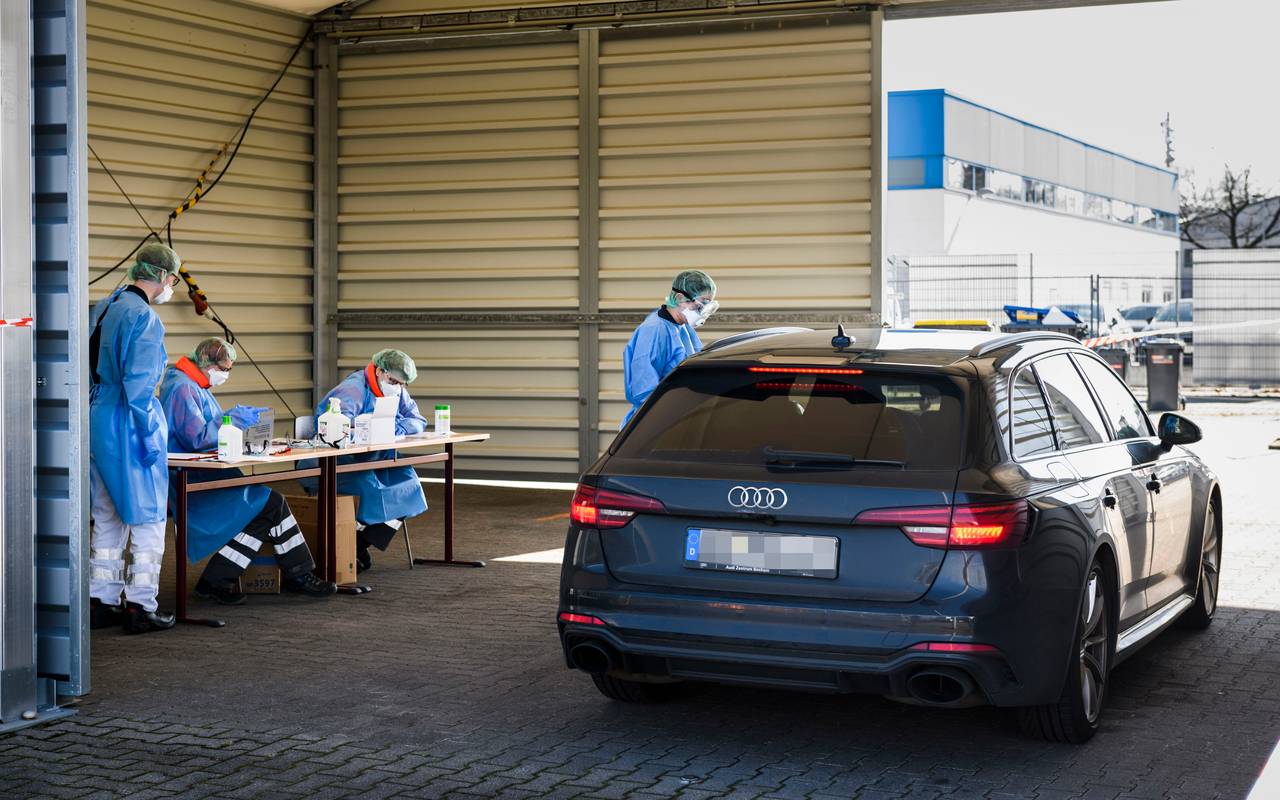 Ein DRK-Mitarbeiter in Schutzkleidung steht in Bochum-Harpen neben einem Auto in der provisorischen Halle der "Drive in"-Teststelle für Corona-Tests