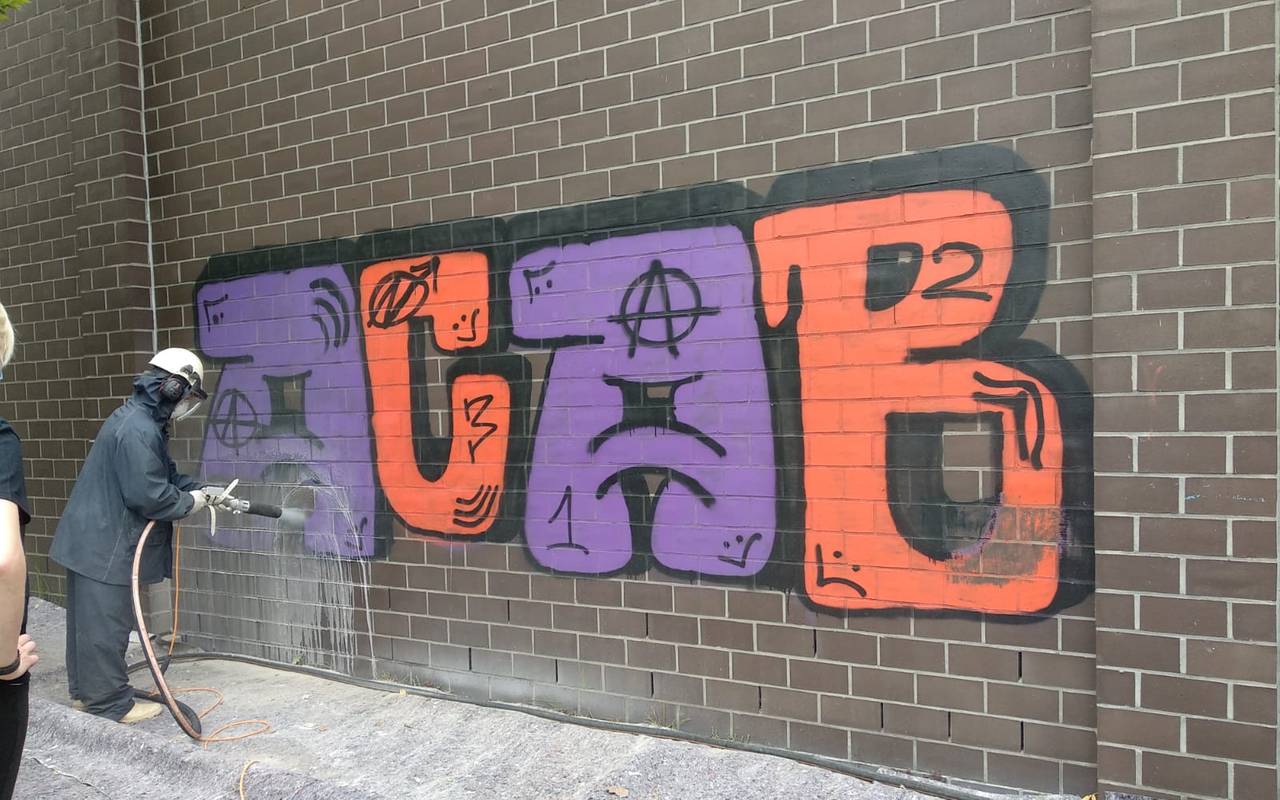 Arbeiter in Schutzkleidung besprüht eine Hauswand, auf der ACAB steht