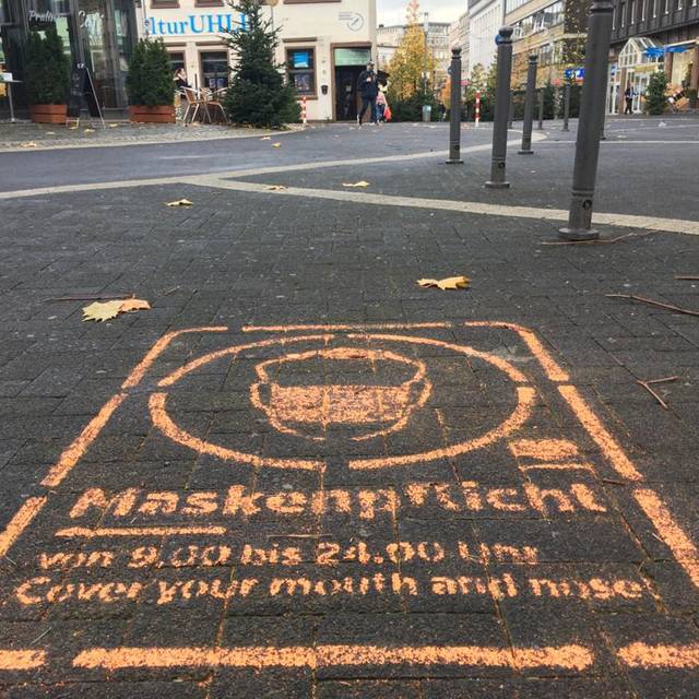 Ein Graffiti auf dem Pflaster der Fußgängerzone weist auf die Maskenpflicht hin.