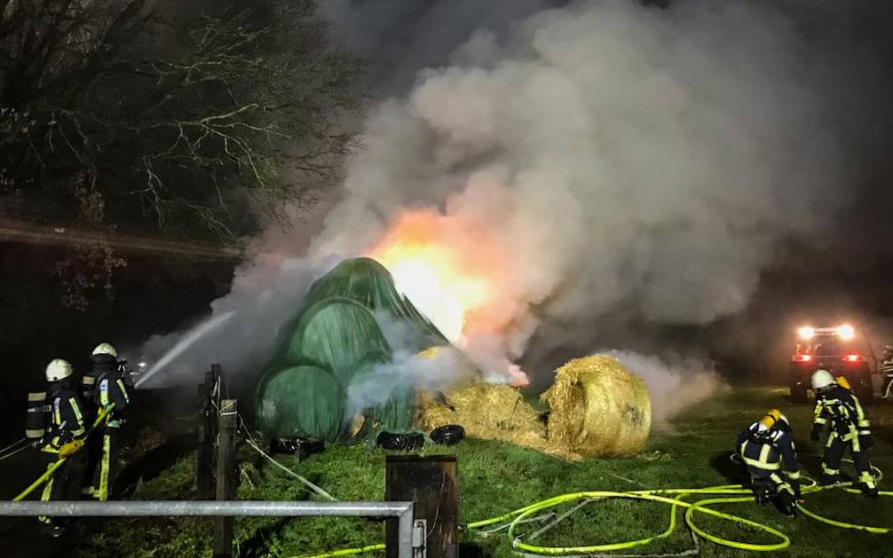Große Rauchwolke zieht aus Strohballen hoch. Die Feuerwehr löscht den Brand.