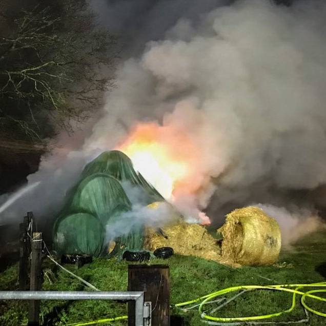 Große Rauchwolke zieht aus Strohballen hoch. Die Feuerwehr löscht den Brand.