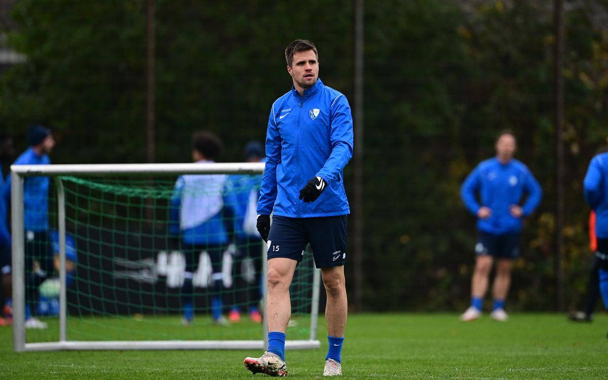 Mann in blauem Trainingsanzug auf einem Fußballplatz.