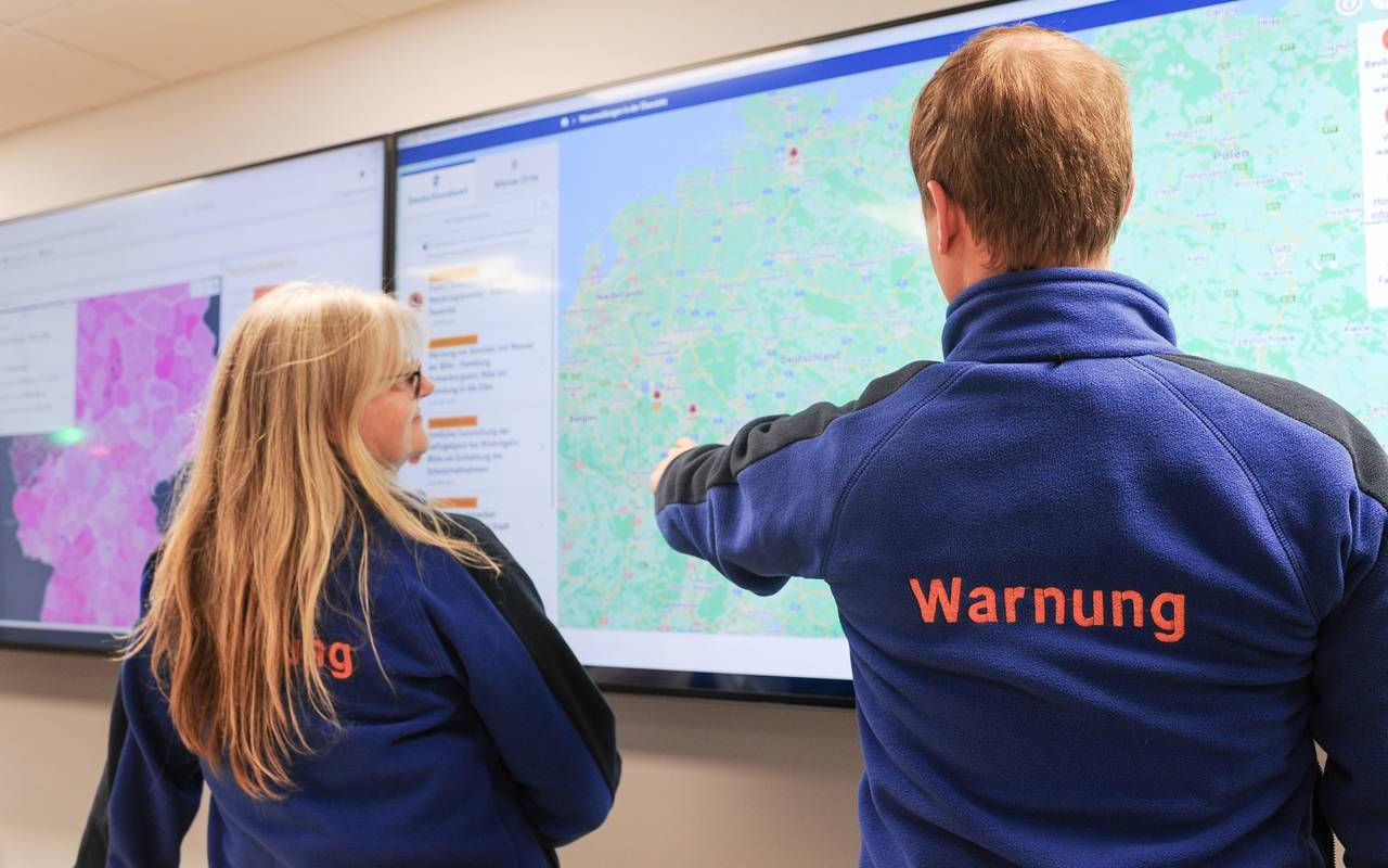 Zwei Personen stehen vor einem großen Bildschirm, der die Deutschland-Karte zeigt. Dies geschieht im Rahmen des bundesweiten Warntags.
