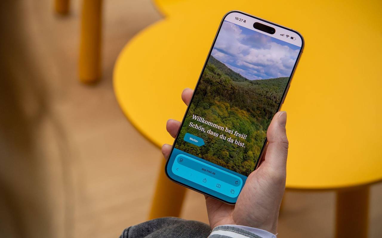 Eine Frau haelt ein Handy mit der Web-App «freii» in der Hand