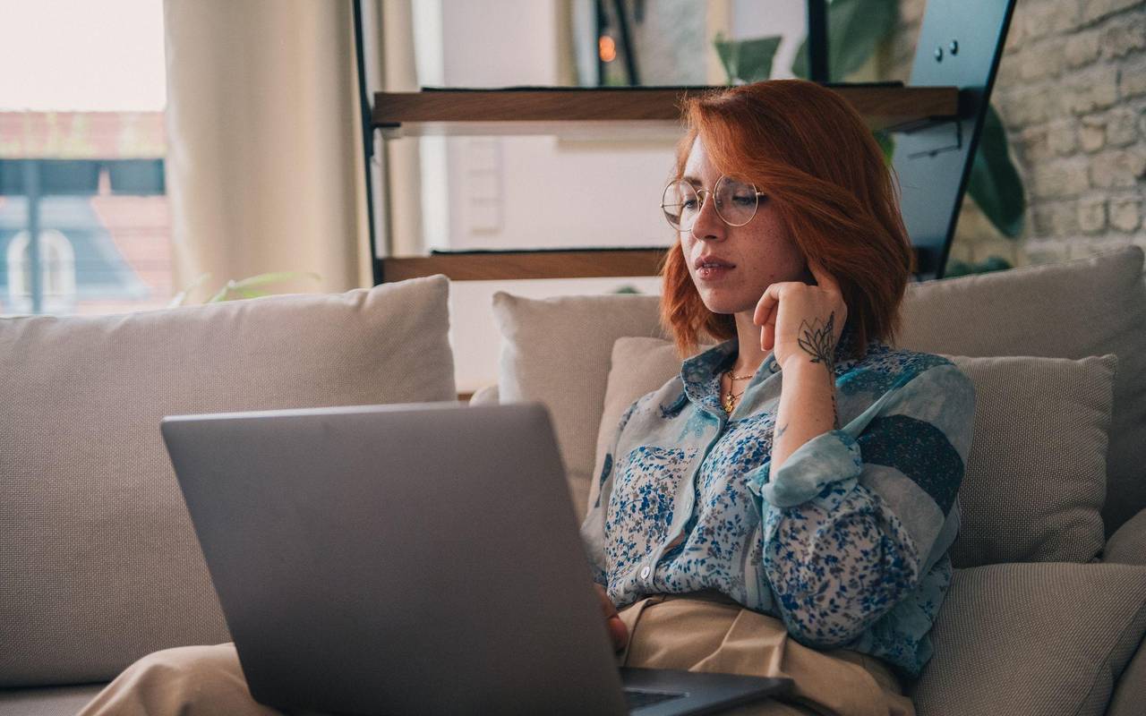Eine Frau sitzt auf der Couch und nutzt einen Laptop