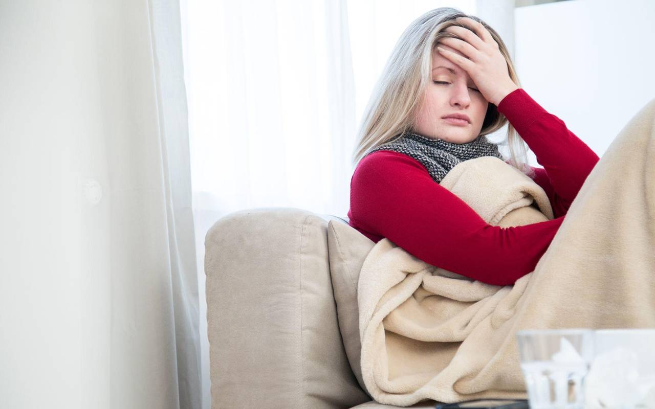 Eine Frau sitzt krank auf einem Sofa