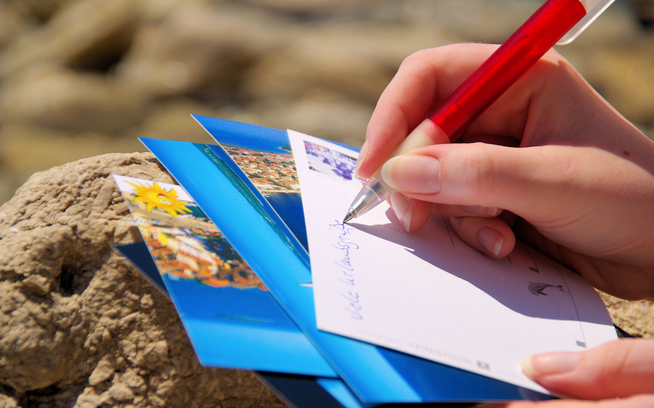Jemand schreibt eine Postkarte mit Urlaubsgrüßen.