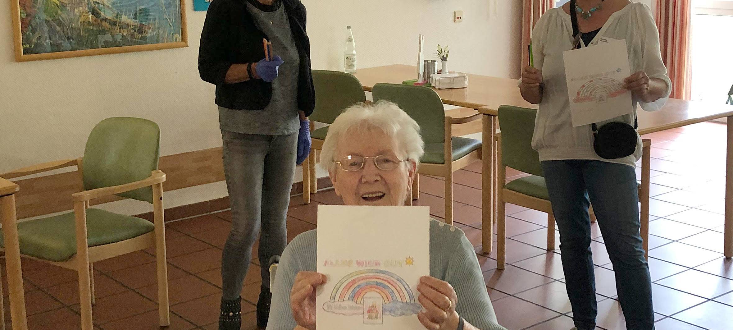 Senioren hält einen Zettel in die Kamera, da ist ein Regenbogen drauf