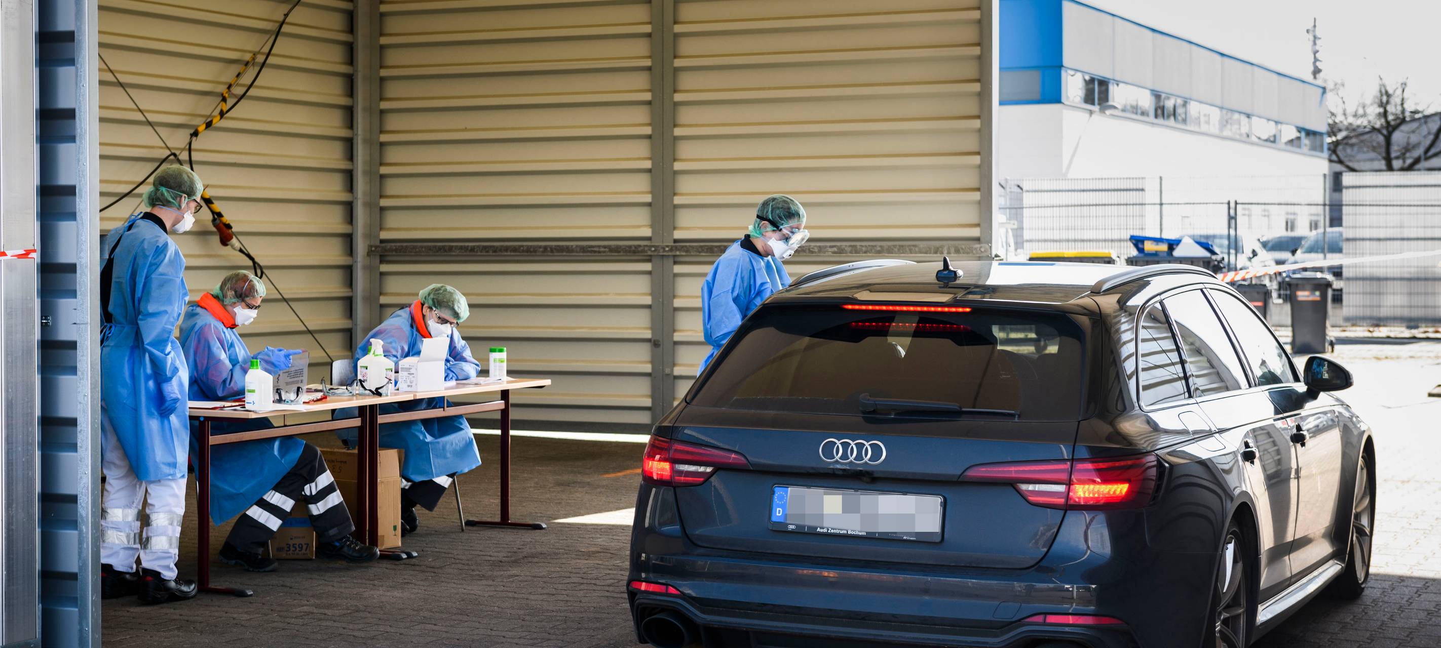 Ein DRK-Mitarbeiter in Schutzkleidung steht in Bochum-Harpen neben einem Auto in der provisorischen Halle der "Drive in"-Teststelle für Corona-Tests