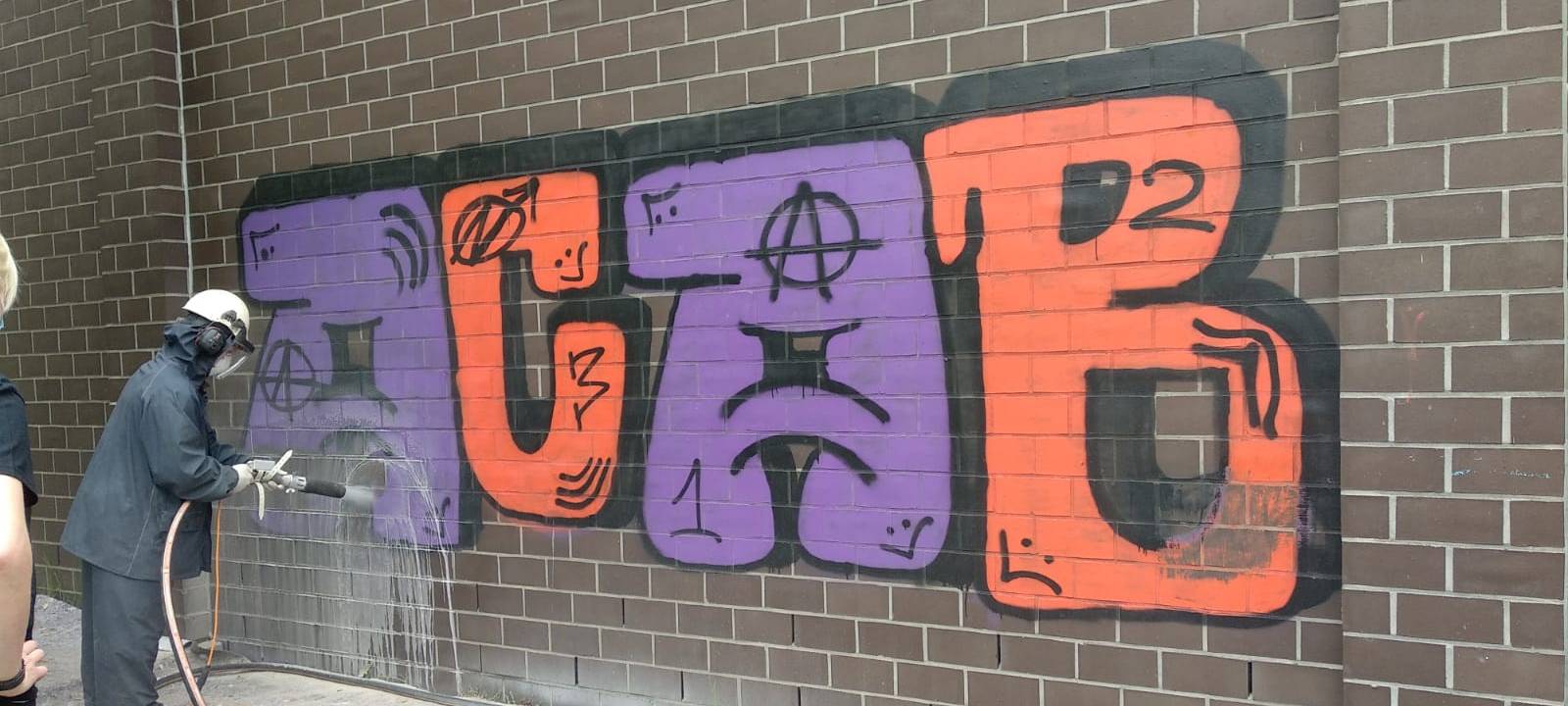 Arbeiter in Schutzkleidung besprüht eine Hauswand, auf der ACAB steht