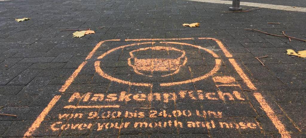 Ein Graffiti auf dem Pflaster der Fußgängerzone weist auf die Maskenpflicht hin.