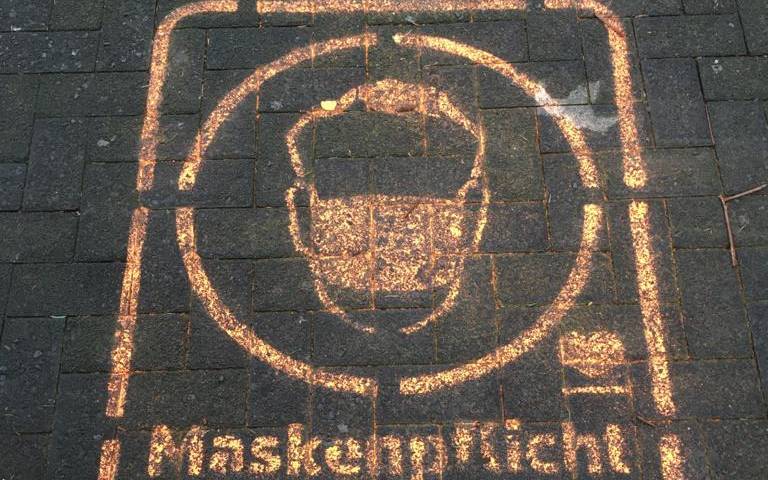 Ein Graffiti auf dem Pflaster der Fußgängerzone weist auf die Maskenpflicht hin.