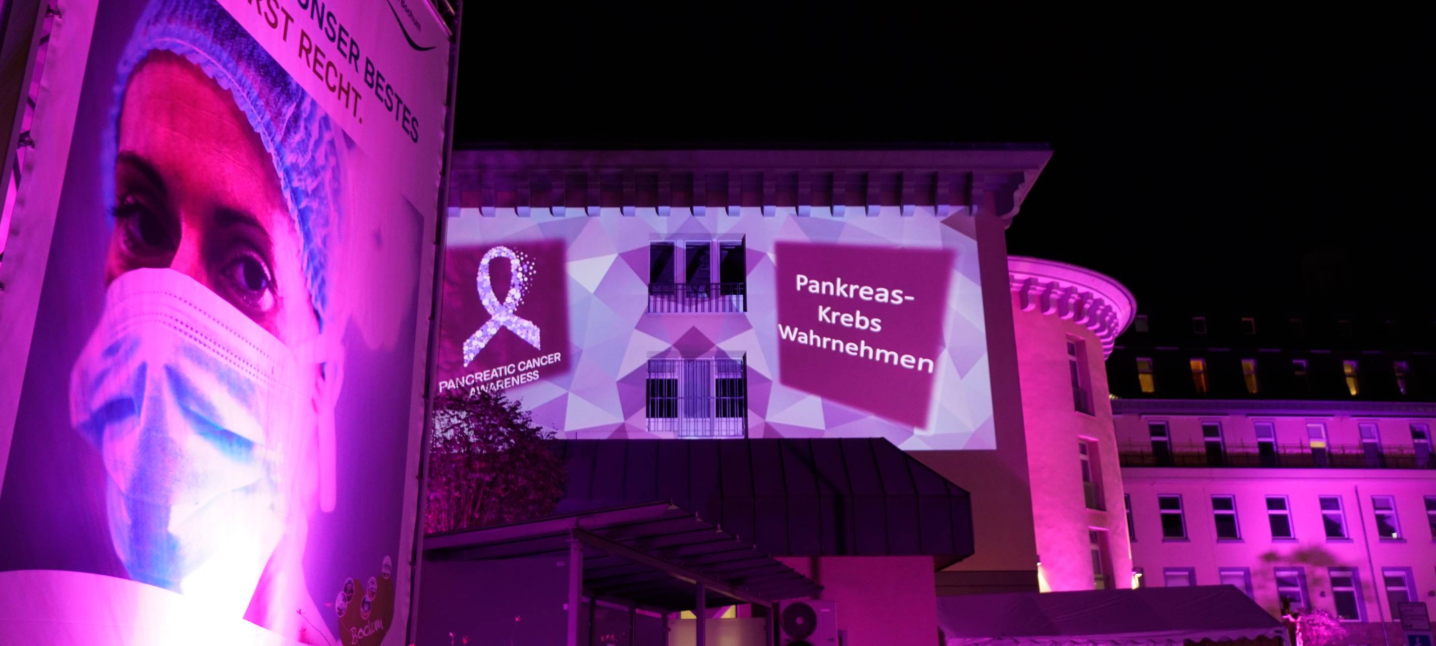 Der Klinikeingang ist lila angestrahlt. Es wird mit Infotexten auf Pankreaskrebs hingewiesen.