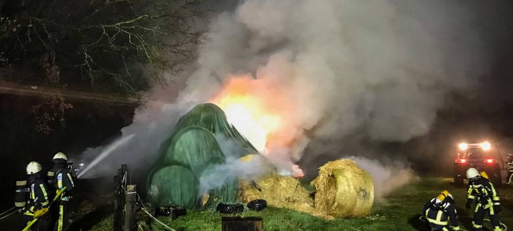 Große Rauchwolke zieht aus Strohballen hoch. Die Feuerwehr löscht den Brand.