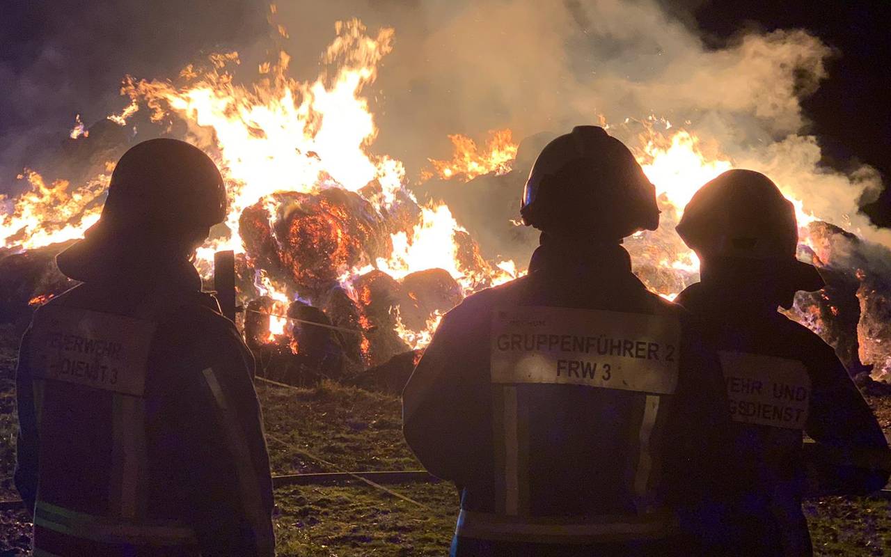 Feuerwehrleute beobachten brennende Strohballen bei Nacht