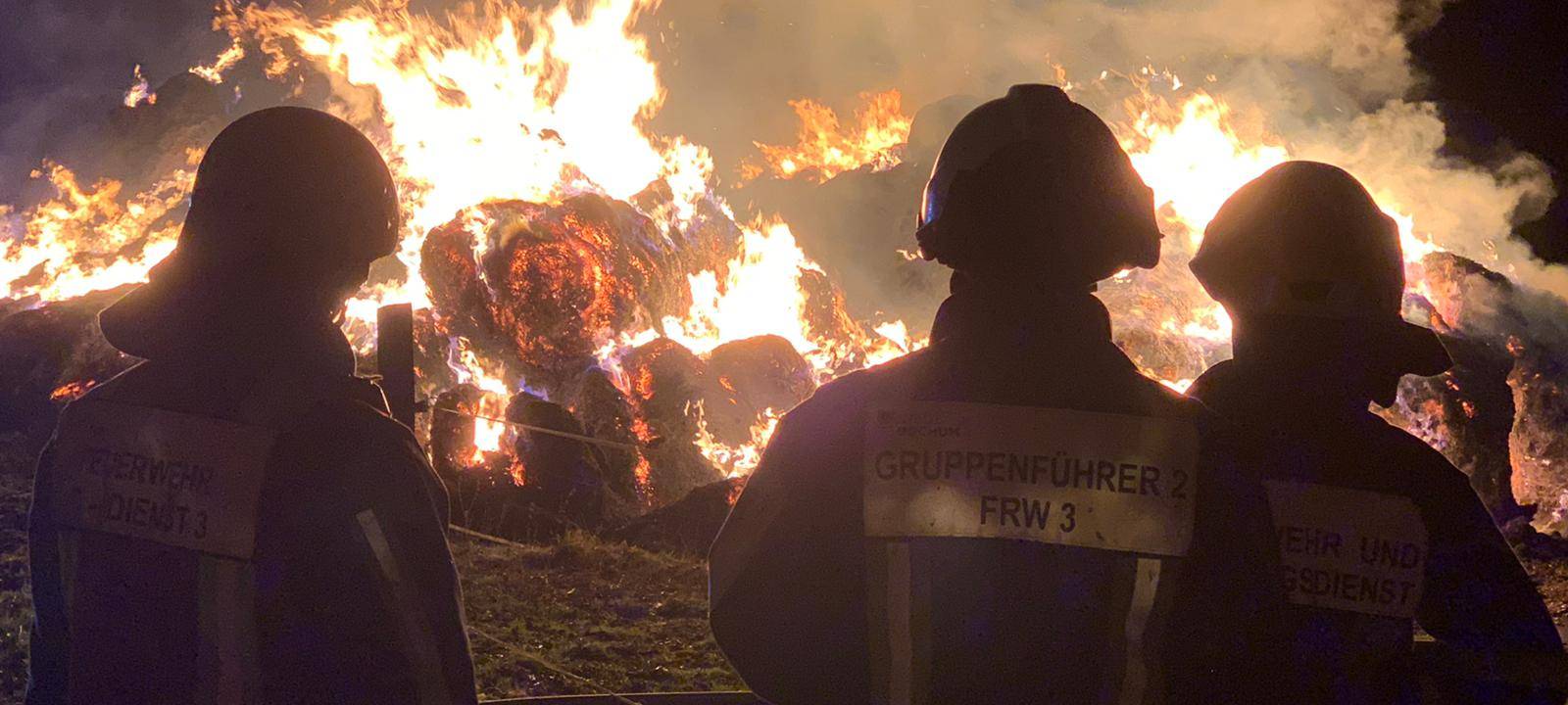 Feuerwehrleute beobachten brennende Strohballen bei Nacht