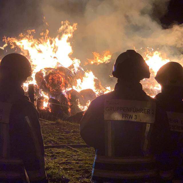 Feuerwehrleute beobachten brennende Strohballen bei Nacht
