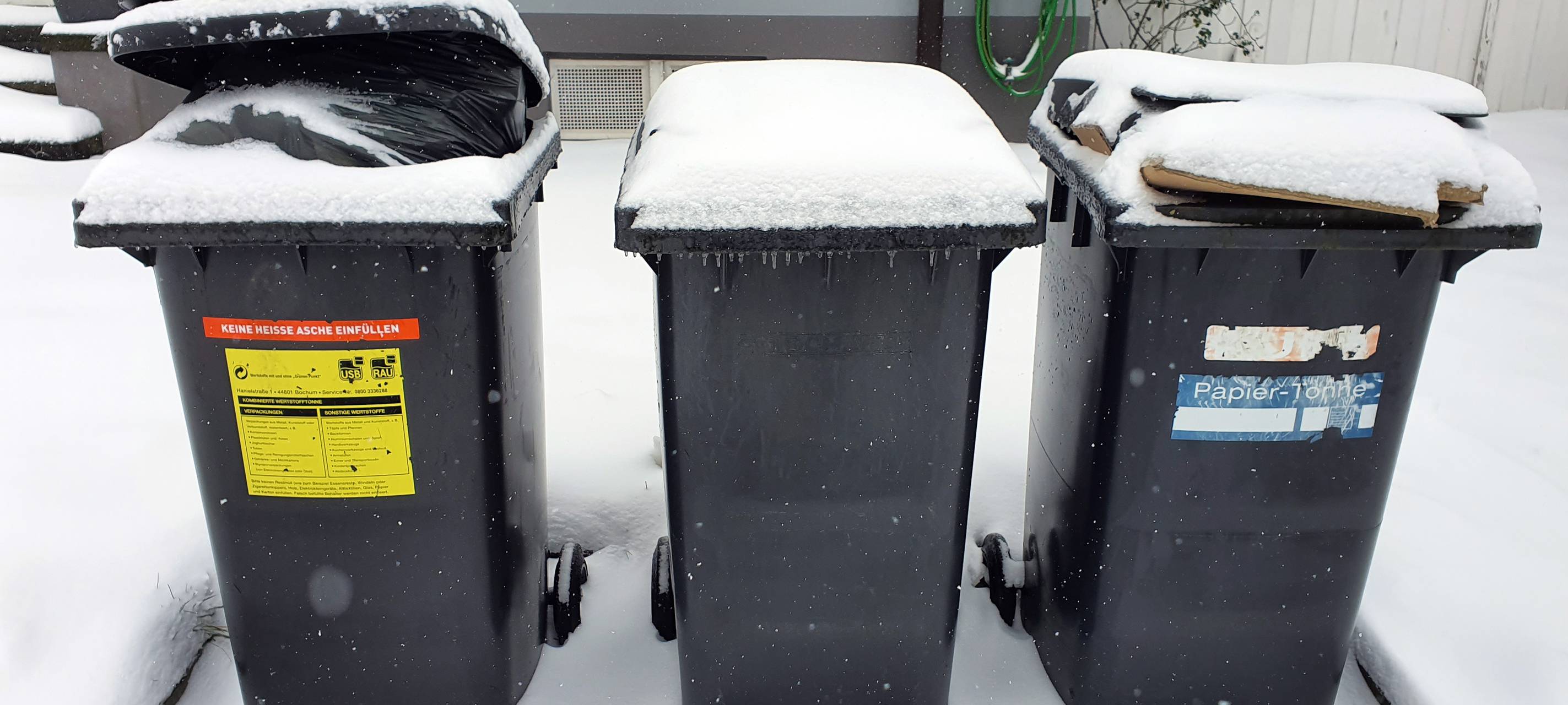 Drei zugeschneite Mülltonnen stehen vor einem Haus