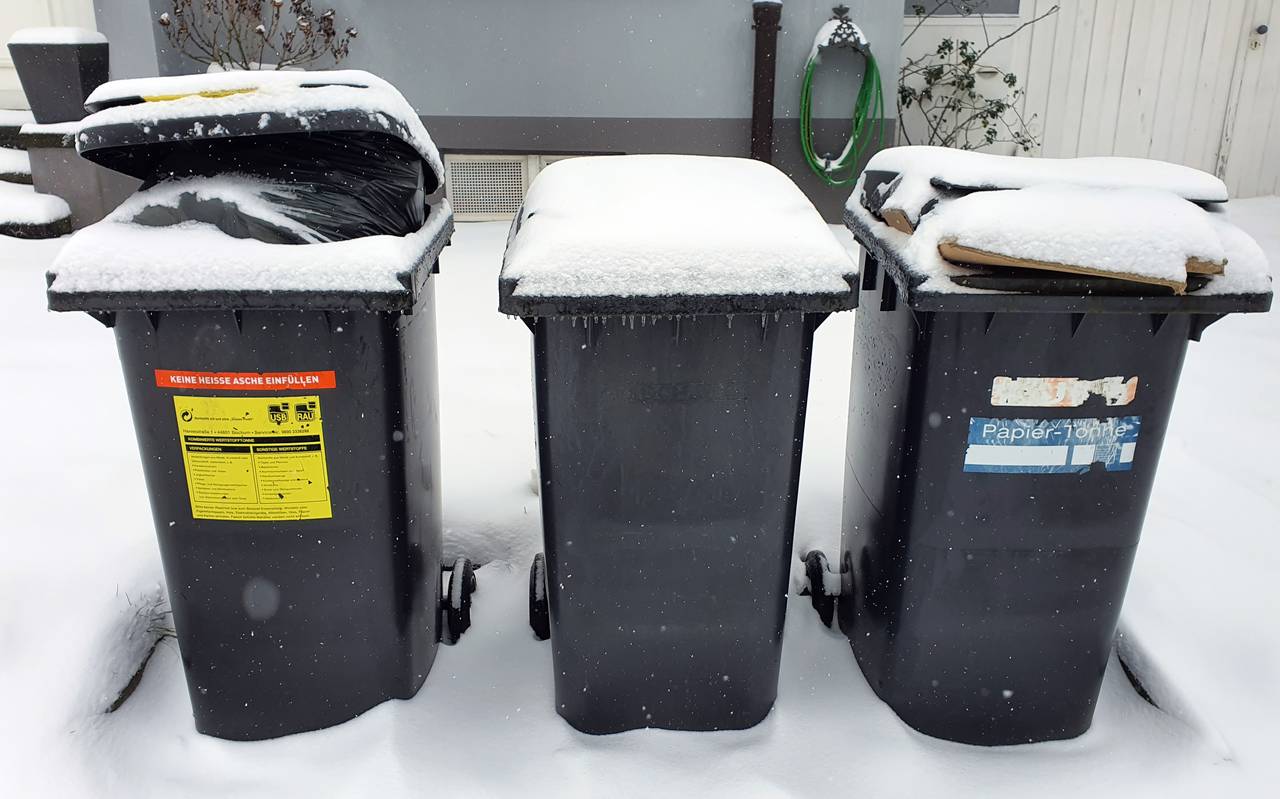 Drei zugeschneite Mülltonnen stehen vor einem Haus