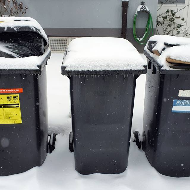 Drei zugeschneite Mülltonnen stehen vor einem Haus
