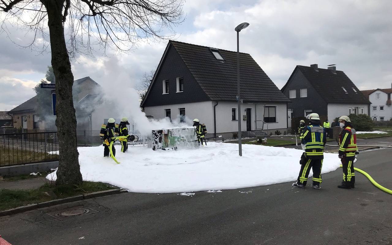 Mehrere Feuerwehrmänner spritzen Schaum auf ein Trafohaus