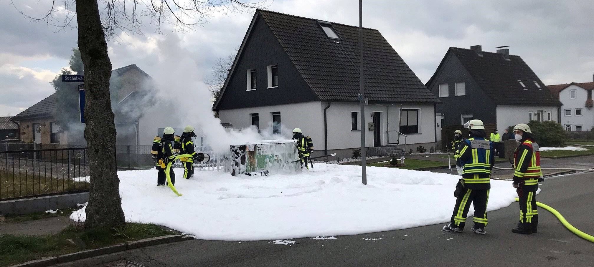 Mehrere Feuerwehrmänner spritzen Schaum auf ein Trafohaus