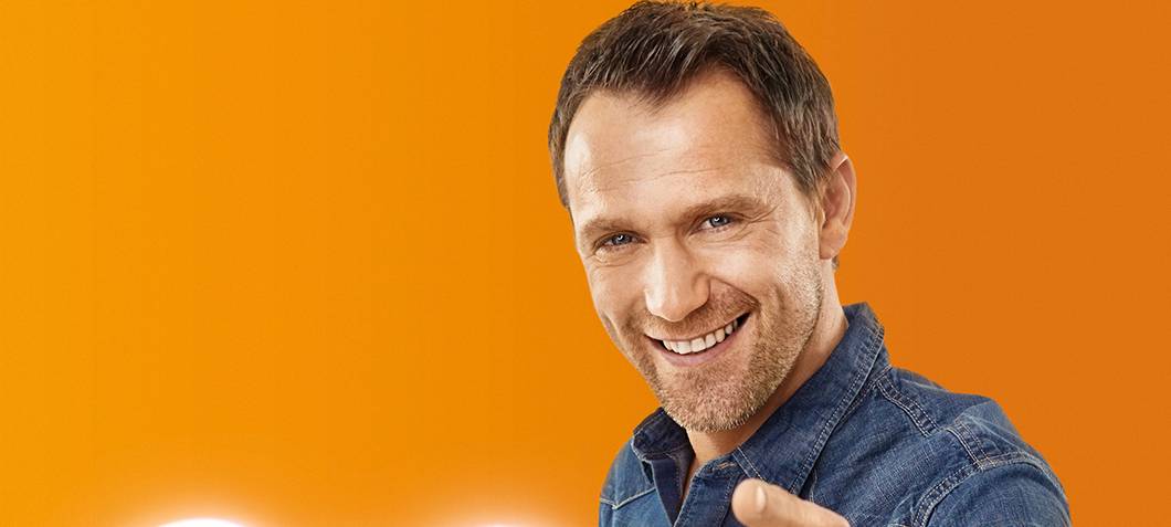 Mann hat ein leuchtendes Herz un der Hand und zeigt freudestrahlend auf den Betrachter