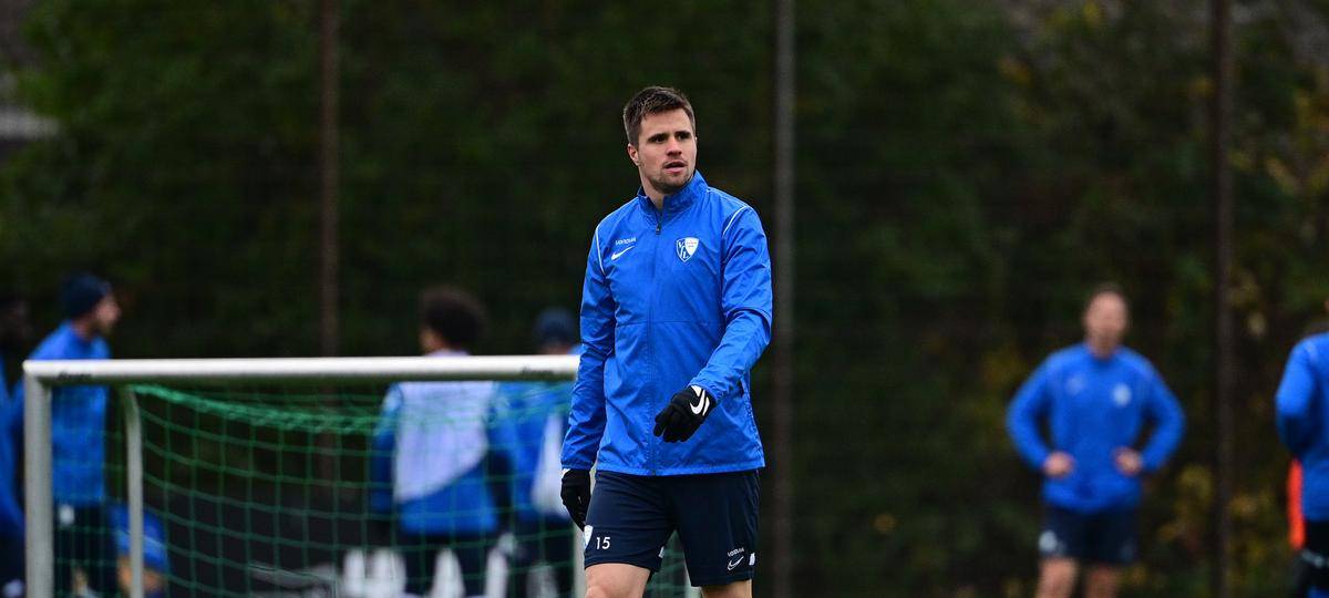 Mann in blauem Trainingsanzug auf einem Fußballplatz.