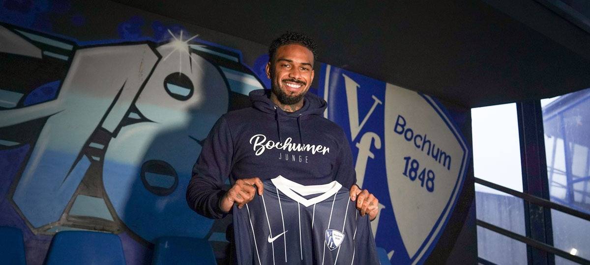 Fußballspieler hält Trikot in der Hand und lächelt in die Kamera