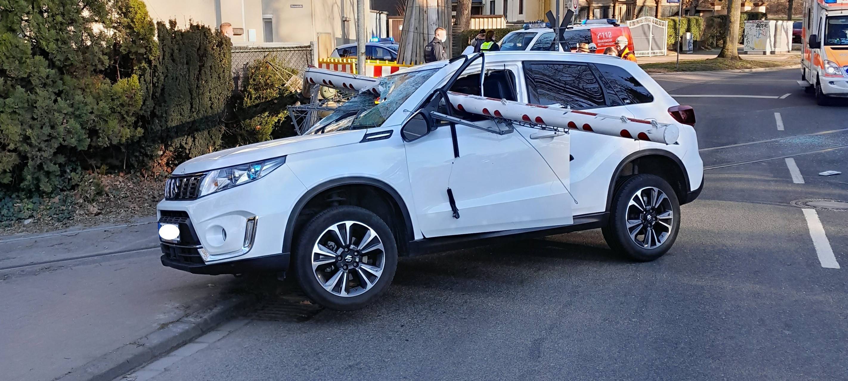 Weißes Auto wird von Bahnschranke im Bereich der Vordersitze durchbohrt