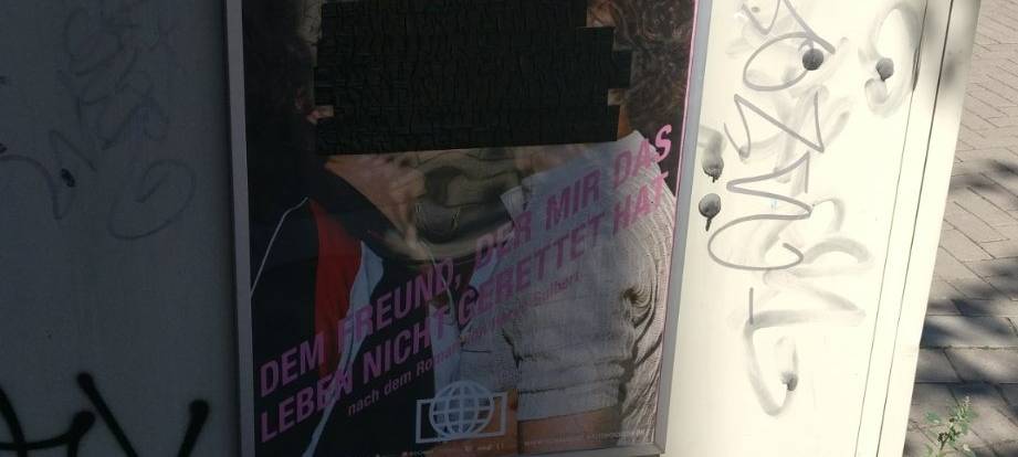 Plakat auf dem sich zwei Männer küssen ist mit schwarzem Tape überklebt