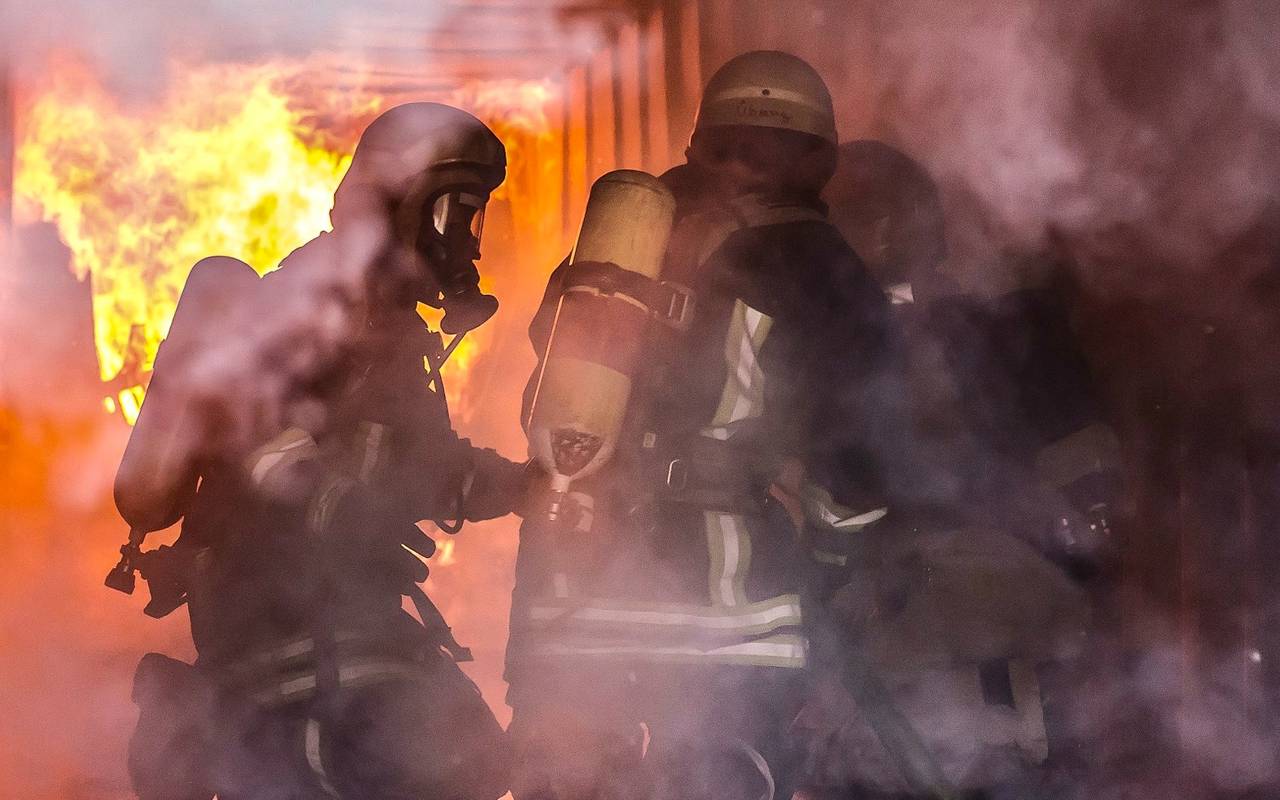 Feuerwehrleute im Einsatz vor einem großen Feuer in einem Keller.
