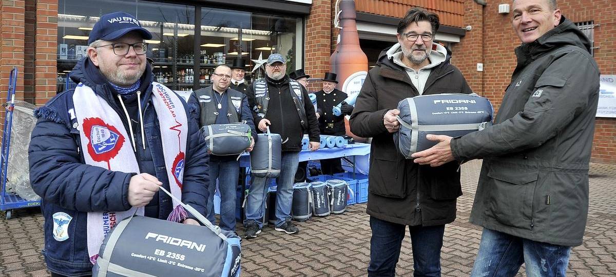 Männer halten Schlafsäcke in der Hand und lächeln in die Kamera.
