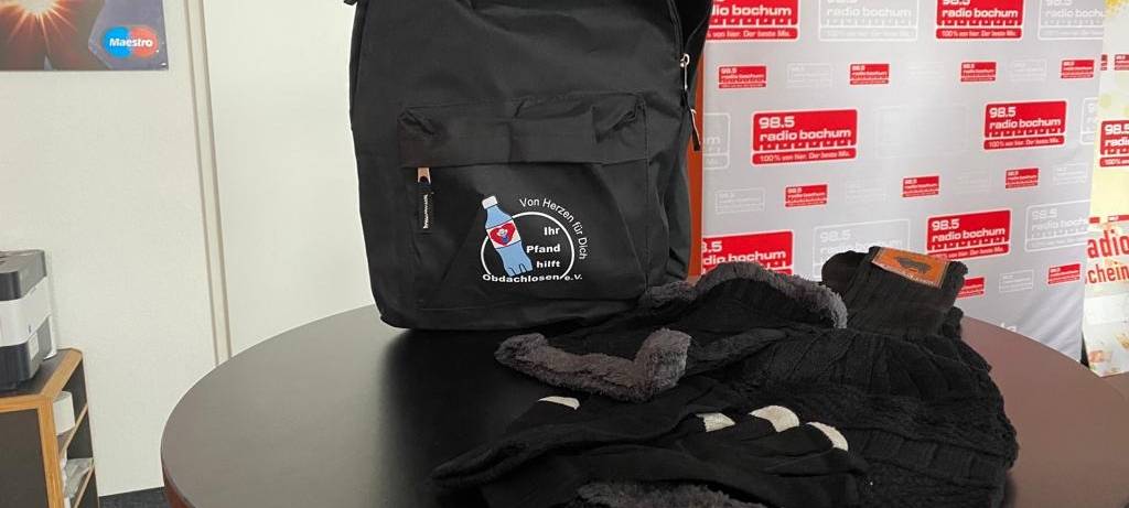 Schwarzer Rucksack, davor liegt schwarze Winterkleidung
