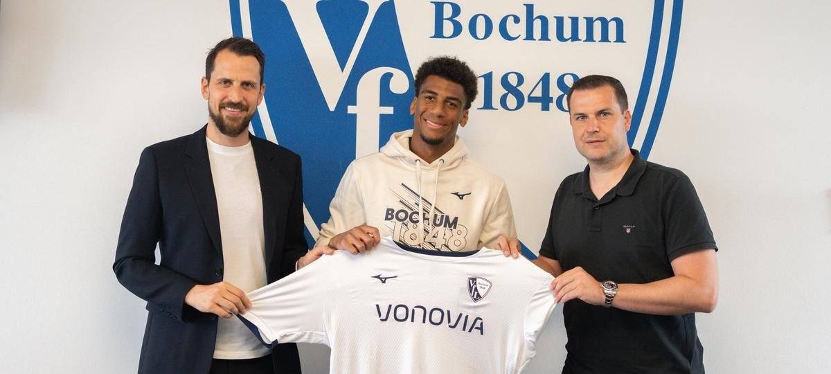 Drei Männer halten ein VfL-Trikot in die Höhe und grinsen in die Kamera