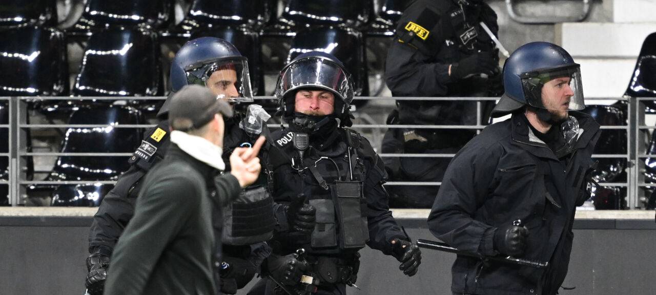 Ein Fußballfan zeigt Polizisten den Mittelfinger, als er an ihnen vorbeiläuft.