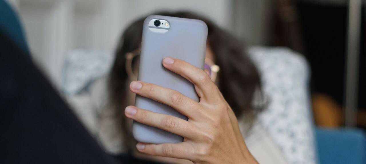 Eine Frau liegt auf einem Sofa und schaut sich ein Video auf der Social-Media-Plattform Instagram auf ihrem Handy an