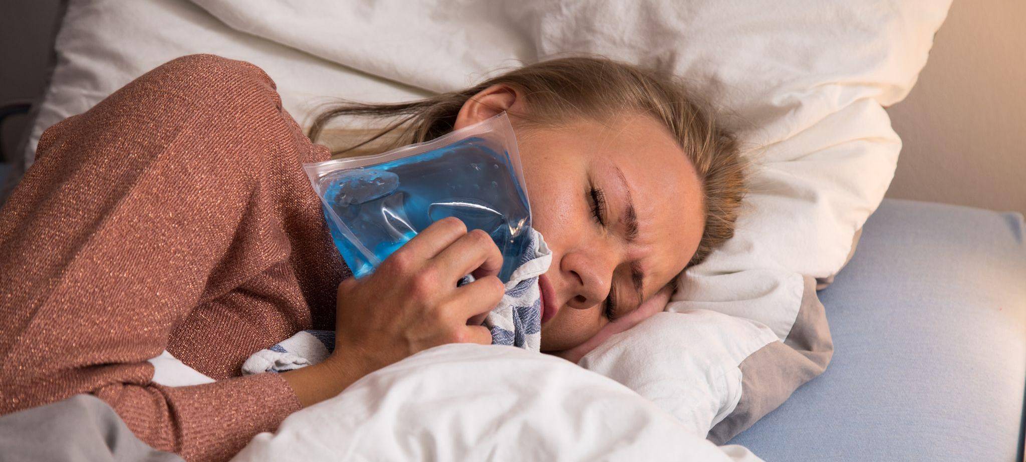 Eine Frau liegt mit Zahnschmerzen im Bett