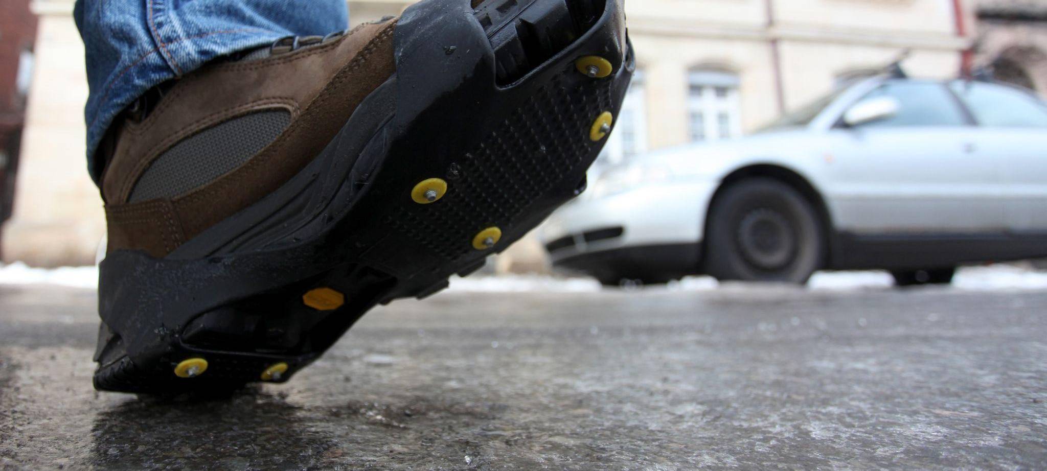 Ein Mann geht mit einer Spikes-Sohle über Eis