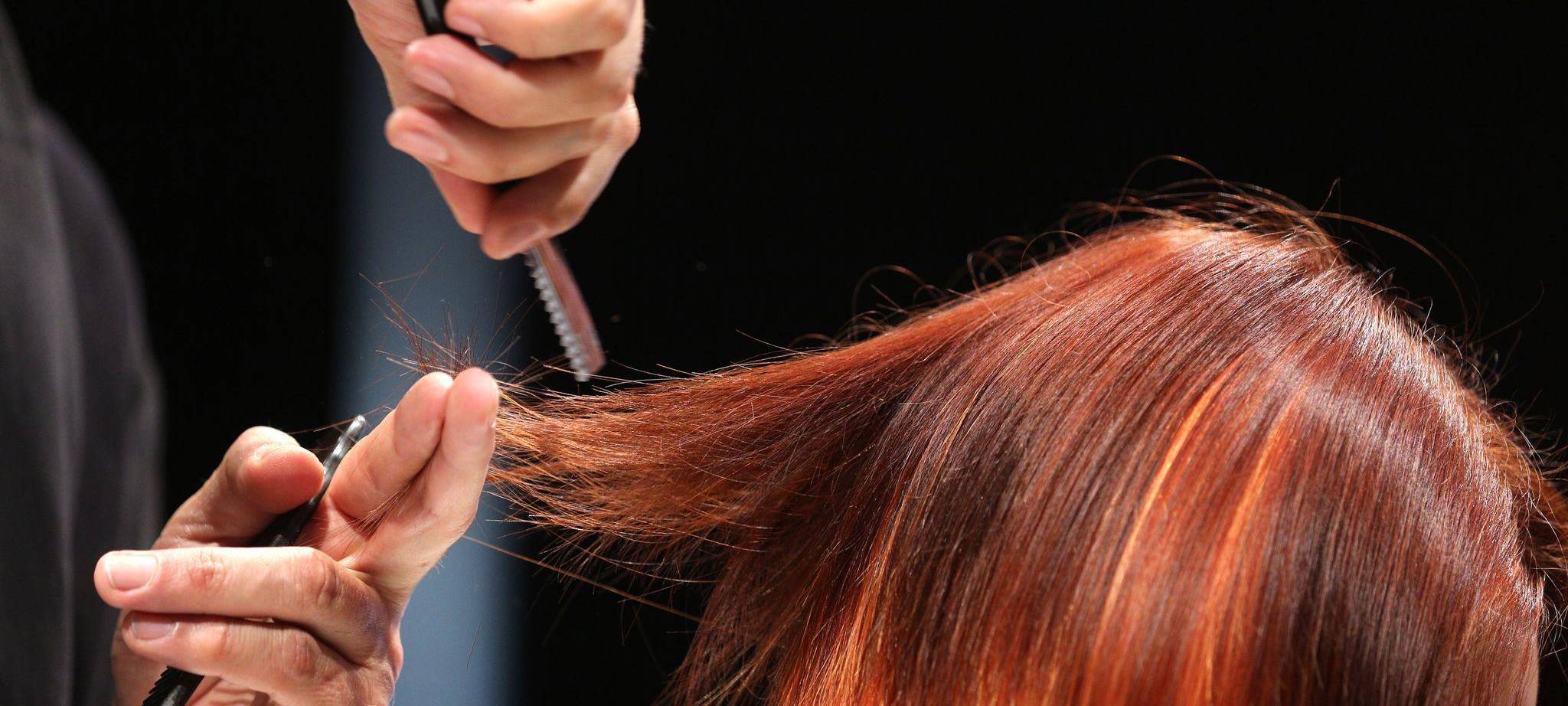 Ein Friseur schneidet einer Frau mit roten Haaren die Haare