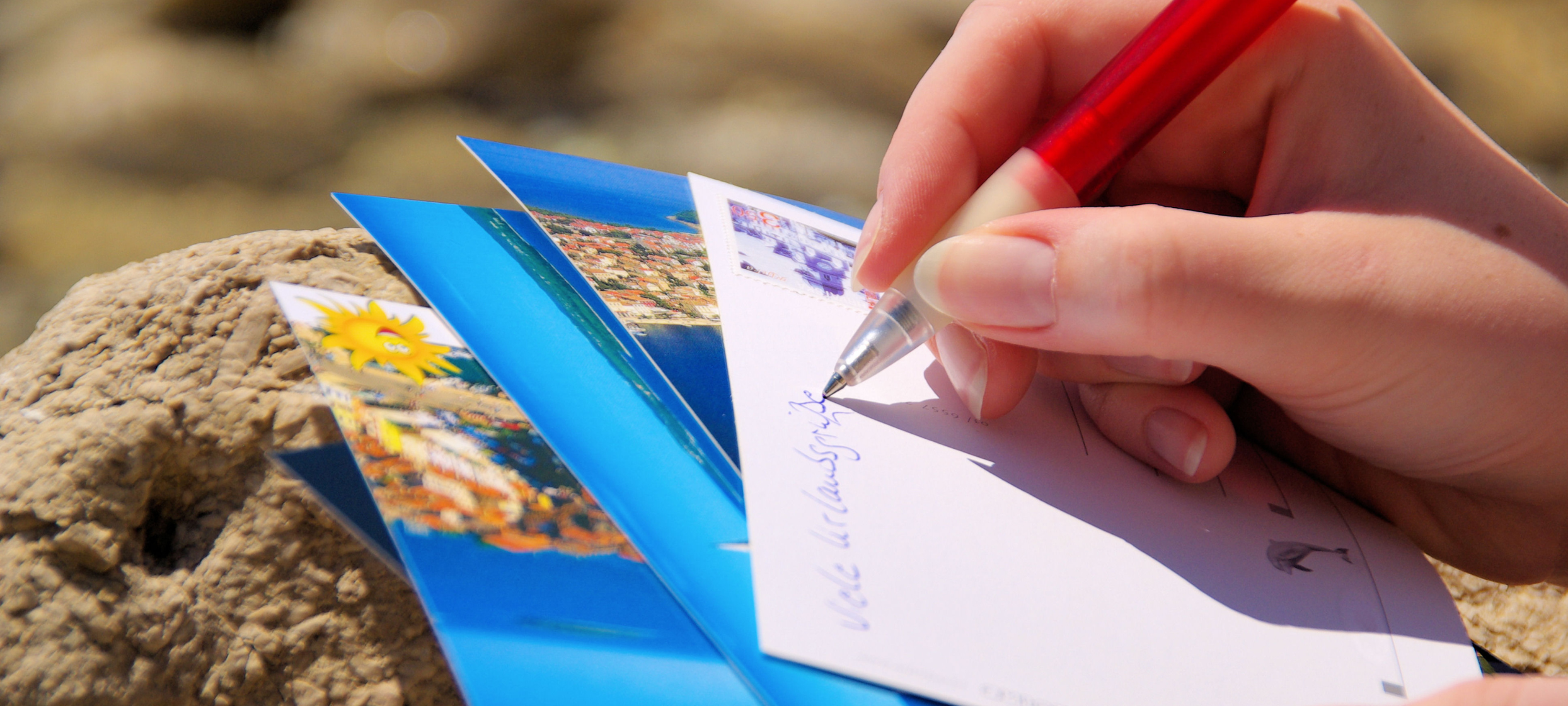 Jemand schreibt eine Postkarte mit Urlaubsgrüßen.
